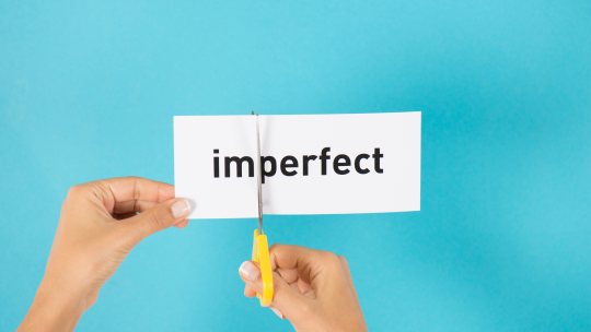 Mani che tagliano un biglietto con sù scritto "imperfect"